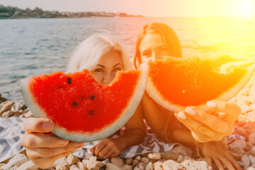 Watermelon Beach Summer: Two women enjoy juicy watermelon slices on a sunny beach during summer...