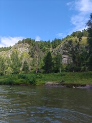 Fototapeta premium Serene River Landscape with Lush Greenery and Rocky Cliffs Under Blue Sky