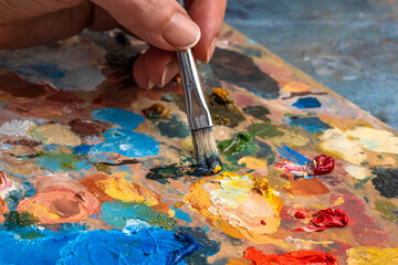 Artist's hands with old used brushes in an artist's studio, palette with multi-colored spots of oil or acrylic paint