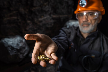 A man showing off his gold nugget find in gold mine, golden vein. Miner wearing a protective helmet...