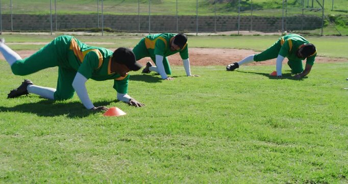 Diverse male baseball teammates are initiating groin-stretch on grassy field marked by cones