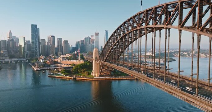 Australia, Sydney: Sydney Harbour Bridge and modern city skyline under sunny morning light, urban infrastructure architecture and road transportation traffic. Drone flight footage aerial panorama