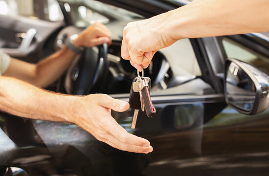 Fototapeta Hands of valet parking worker giving key to driver man sitting inside car. Unrecognizable man buyer taking key from brand new automobile at autosalon showroom. Car buying, renting