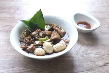 braised pork tendon and meatball with bean sprout toping fresh basil in brown soup on bowl dipping...