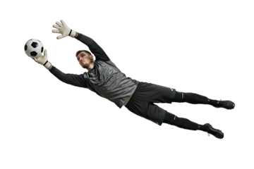 A determined male soccer goalkeeper, clad in a grey jersey and black shorts, bravely dives to catch the ball mid-air against a pure white background