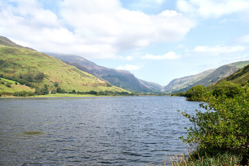 Scenic view of a mountain valley with a lake in the foreground, green slopes and cloudy summer sky...