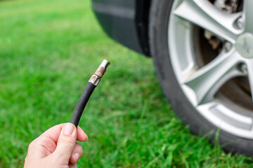 Hands are shown connecting a compressor hose to a car tire valve in a grassy residential area....