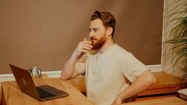 A male yoga mentor is sitting at a table and typing on a laptop