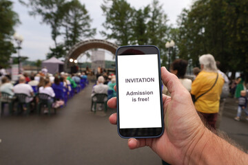 Hand holding smartphone showing free admission invitation to open air concert