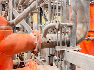 A row of orange industrial batch screens and pumps in a factory, with complex piping systems and motors. The machinery is part of a large-scale manufacturing or processing plant.