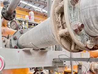 A detailed shot of a large industrial pipe and flange connection, showing rust and dust accumulation. A pressure gauge is visible, highlighting a key component of the industrial system.
