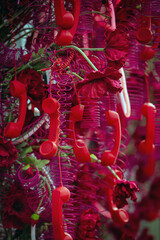 Vibrant installation featuring red telephone handsets and coiled cords intertwined with deep pink flowers, creating a surreal and colorful composition