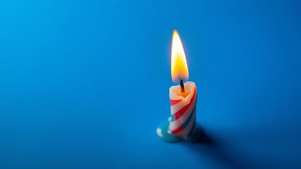 A single colorful birthday candle with melting wax, casting a warm glow on deep blue.