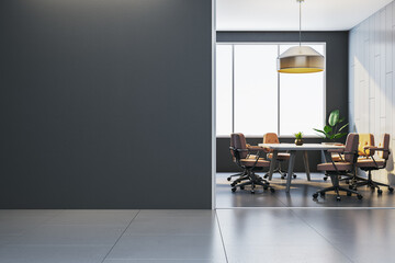 Modern office interior with blank dark wall and sunlit meeting room featuring chairs and table,...
