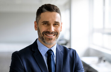 Portrait of happy confident middle aged businessman in suit looking and smiling at camera, posing...