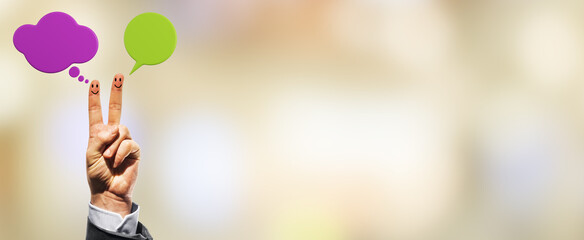 Two fingers with smiley faces and colorful speech bubbles raised in peace sign on blurred...