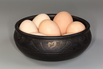 Boiled light brown eggs in black clay bowl, side view