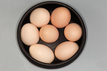 Boiled light brown chicken eggs in black bowl, top view