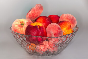 Flat peaches and nectarines in glass bowl on gray surface