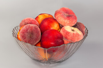 Flat peaches and nectarines in glass bowl on gray surface