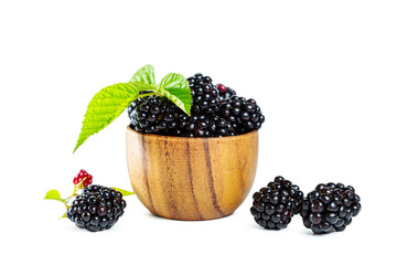 Ripe shiny blackberries with leaves in a wooden bowl isolated on a white background.