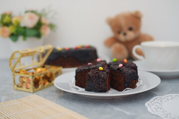 Chocolate cake slices on a white plate with decorations, next to a chest with gold and a cup of coffee