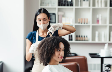 Hairdresser in protective mask cutting hair of curly african american client in beauty salon, free...