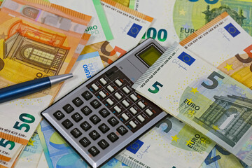 A ballpoint pen and a calculator are partially visible between European Union banknotes