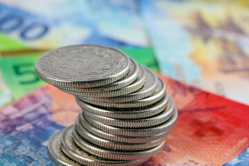 A stack of coins arranged crookedly on top of Swiss franc banknotes