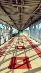 Fototapeta premium Modern covered and empty railway overbridge pathway with perspective leading lines and patterned floor. Transportation infrastructure, pedestrian walk, urban design, geometric shadows
