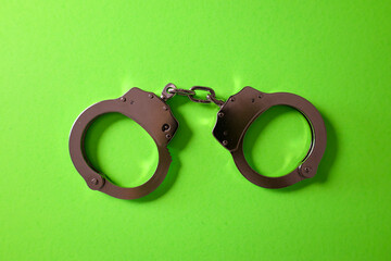 Silver handcuffs on green background