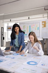 Positive multiethnic office colleagues analyzing paper sales reports, marketing research results...