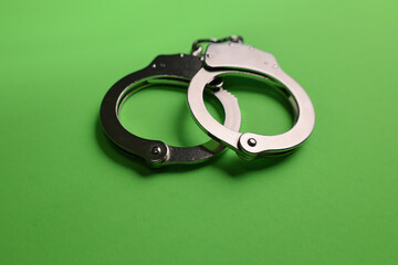 Silver handcuffs on green background