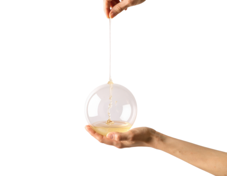 Two hands interact with a glass sphere filled with viscous golden liquid being stretched.