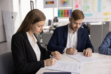Two young business partners signing contract on meeting in office, getting agreement after...