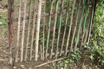 A handmade bamboo fence gate tied with ropes, standing amidst green plants and soil, reflecting rural craftsmanship, simplicity, and natural living.