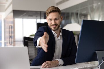 Positive confident handsome young business leader man giving hand for shaking at camera, sitting at...