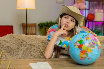 Young child girl sitting at home table wears a travel hat and inflatable ring while looking at a...