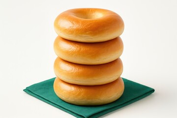 Four freshly baked bagels stacked vertically on a green napkin with a plain white background