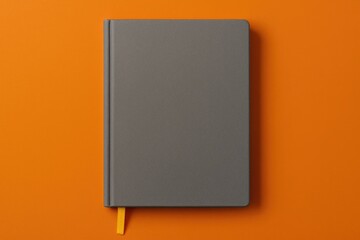 Overhead shot of a grey notebook featuring a yellow bookmark set against an orange surface