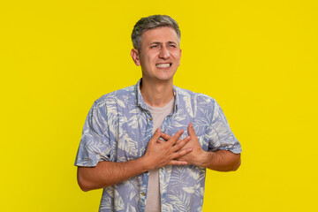 Middle-aged man grabbing chest with painful grimace leaning forward in sudden intense discomfort...