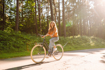 Young woman riding a bicycle on a path in a dense sunny forest. Happy woman enjoying nature and...