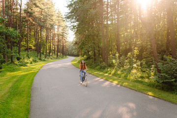 Young woman riding a bicycle on a path in a dense sunny forest. Happy woman enjoying nature and...