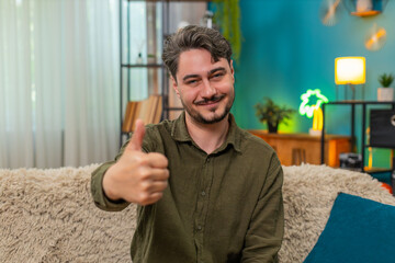 Middle-aged man at home lifts thumb up smiling showing like sign positive feedback success. Young...