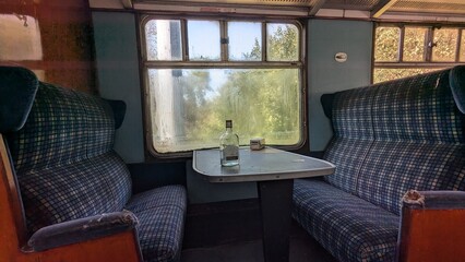 Abandoned train carriage benches and table with unbranded bottle, window condensation, torn seat,...