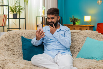 Indian man at home gets amazing smartphone message eyes widen shouts wow celebrates victory pure...