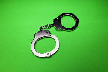 Silver handcuffs on green background