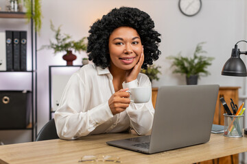 African American businesswoman at home office slowly sips coffee gazing out window letting ideas...