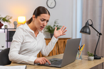 Young businesswoman at home office stares at frozen laptop presses keys and waits tense with sigh....