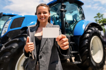 Businesswoman holding business card in front of tractor